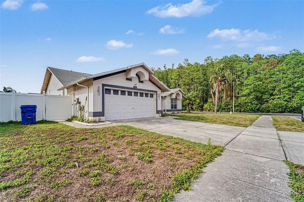 A single-story house with a white garage door, concrete driveway, and a white privacy fence — 8511 SIAMANG COURT, NEW PORT RICHEY, FL