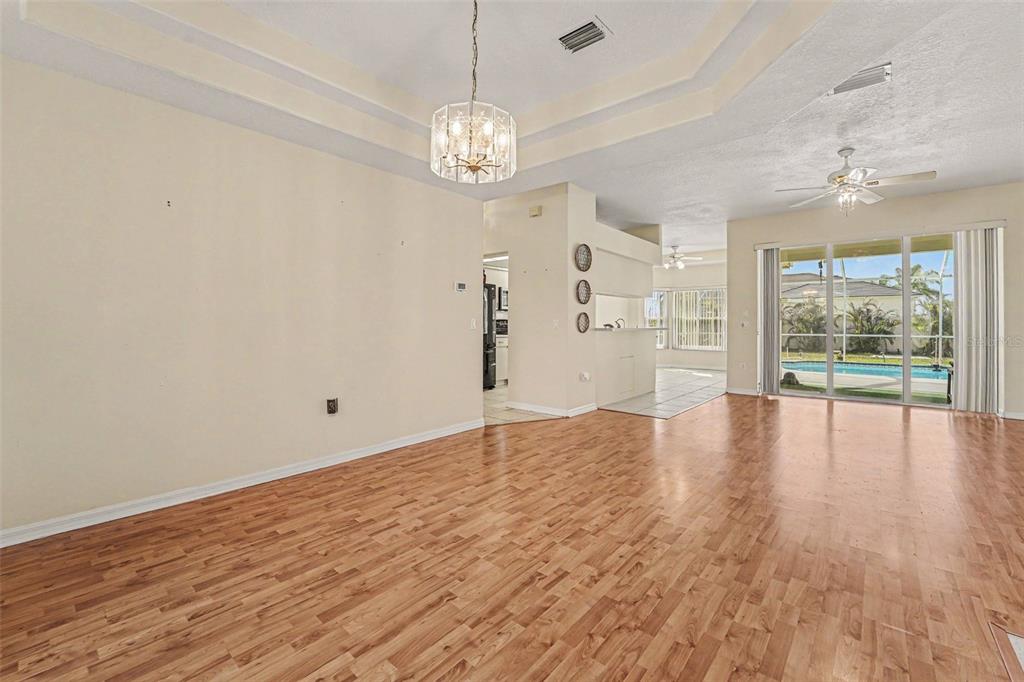 A spacious living room with wood-look flooring, a tray ceiling, and sliding glass doors — 8511 SIAMANG COURT, NEW PORT RICHEY, FL