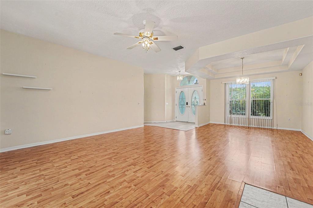 A spacious living room features light-colored walls, wood-look flooring, a ceiling fan, and double doors — 8511 SIAMANG COURT, NEW PORT RICHEY, FL