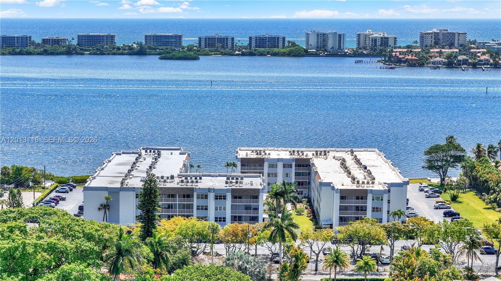 An aerial view shows a multi-story apartment complex situated along a large body of water — 1516 S Lakeside Dr # 105, Lake Worth FL 33460, LAKE WORTH, FL