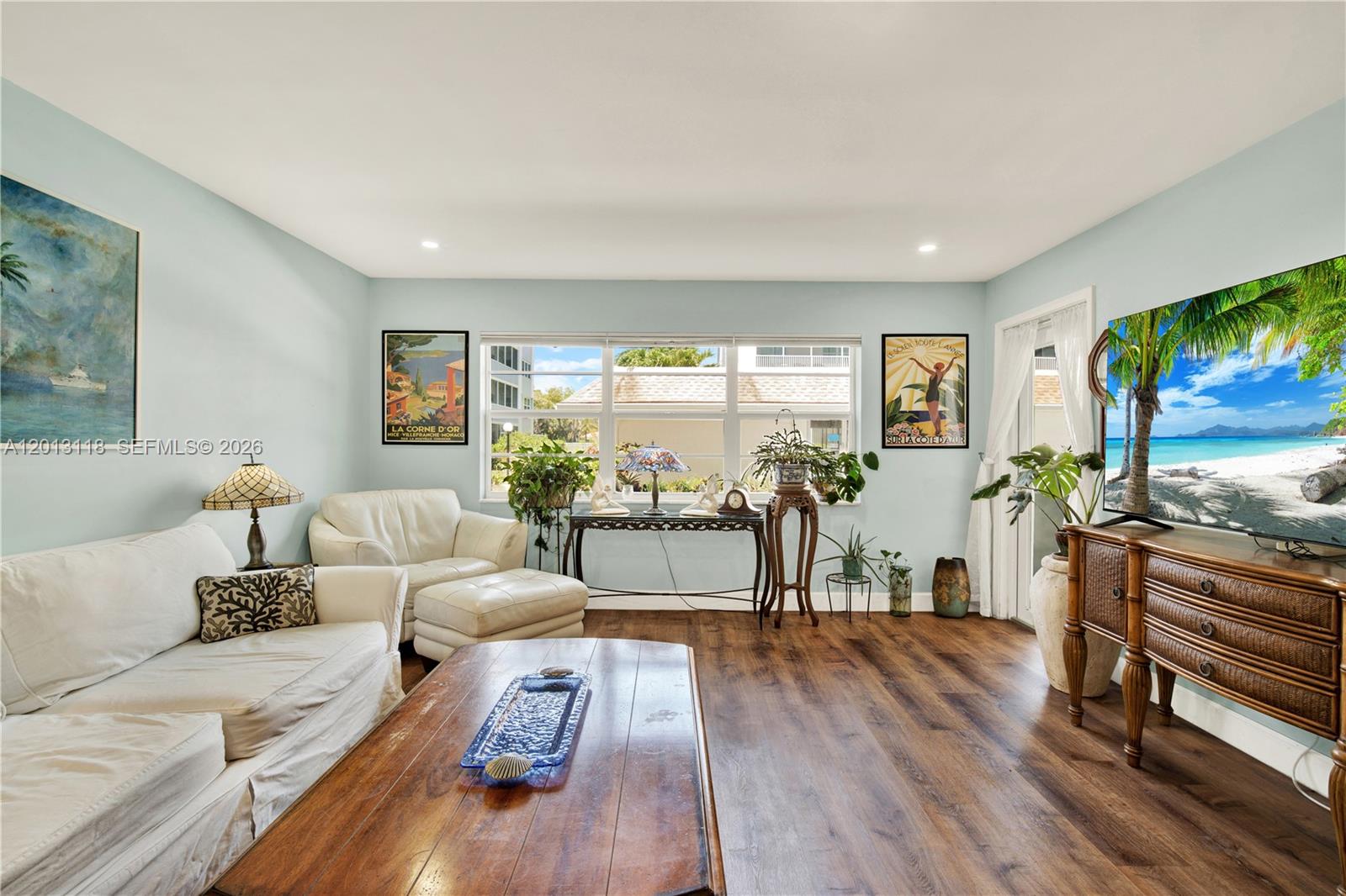A living room features light blue walls, wood-look flooring, a white sofa, and a television — 1516 S Lakeside Dr # 105, Lake Worth FL 33460, LAKE WORTH, FL