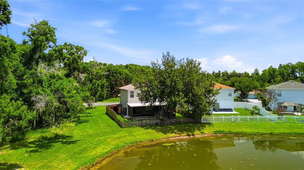 A two-story house with a screened porch sits behind a fence next to a pond — 9913 EDMONTON DRIVE, LAND O LAKES, FL