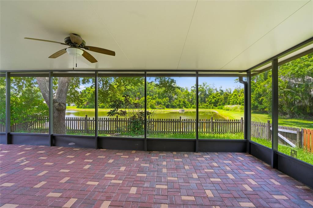 A screened-in patio with a brick paver floor overlooks a pond and a wooden fence — 9913 EDMONTON DRIVE, LAND O LAKES, FL