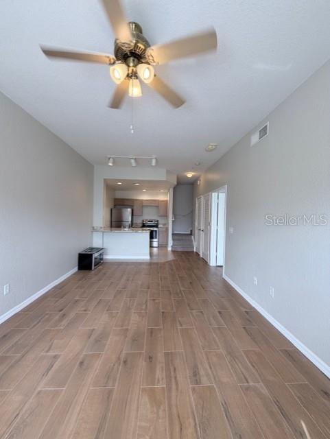 An open-concept living area features wood-look tile flooring, a ceiling fan, and a kitchen beyond — 2201 SAN VITTORINO CIRCLE UNIT 106, KISSIMMEE, FL