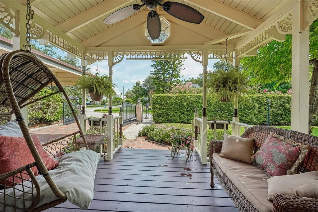 A covered wooden porch features a hanging chair, wicker sofa, ceiling fan, and garden views — 1020 VENETIAN AVENUE, ORLANDO, FL