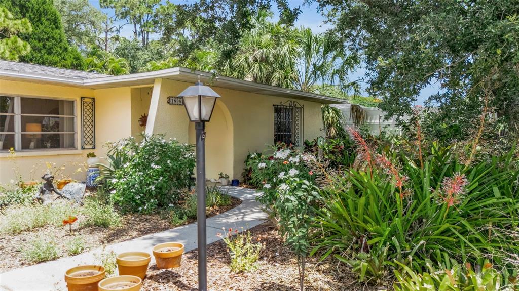 A light-colored house exterior features a front walkway, a lamp post, and lush garden landscaping — 1808 49TH STREET W, BRADENTON, FL