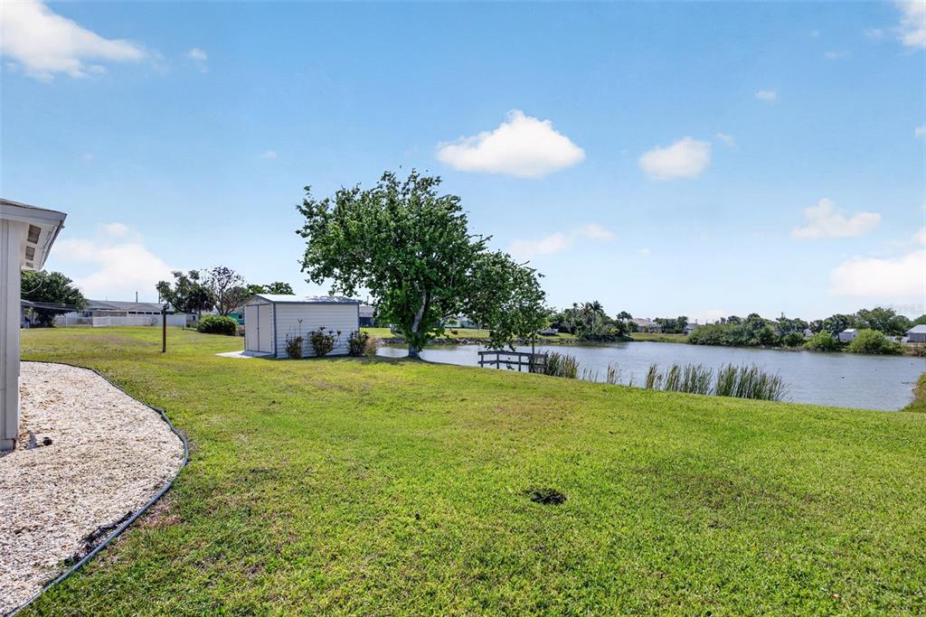 A grassy backyard features a small shed, a large tree, and a pond — 1255 LINCOLN DRIVE, ENGLEWOOD, FL