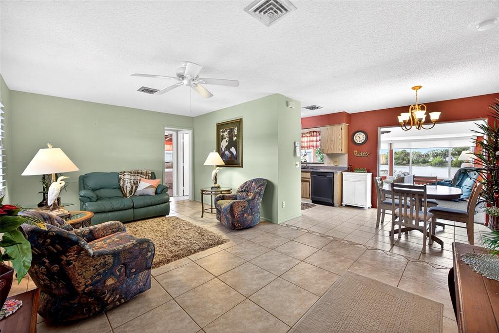 A living room with tile floors, a green sofa, patterned armchairs, and an adjacent dining area — 1255 LINCOLN DRIVE, ENGLEWOOD, FL