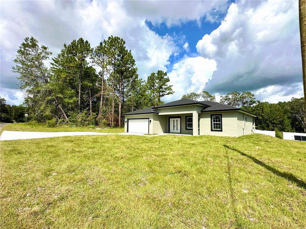 A single-story house with a garage and light-colored exterior sits on a grassy lot — 8010 N POCONO DRIVE, CITRUS SPRINGS, FL