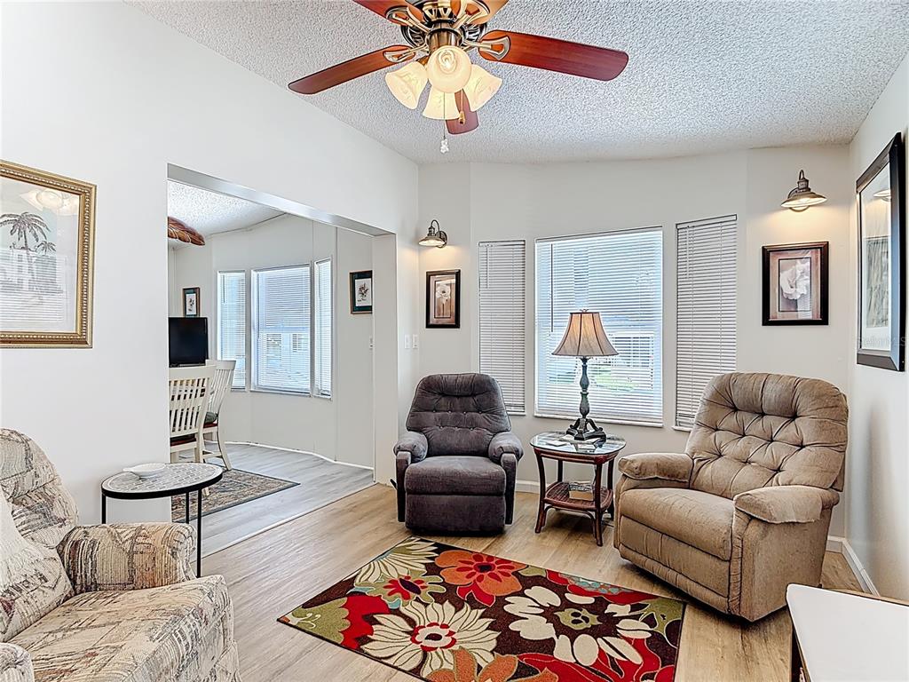 A living room features a ceiling fan, two recliners, a floral rug, and wood-look flooring — 9000 US HWY 192 # 545, CLERMONT, FL