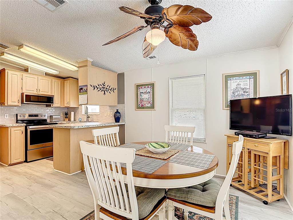 A kitchen and dining area featuring a round wooden table, ceiling fan, and light cabinetry — 9000 US HWY 192 # 545, CLERMONT, FL