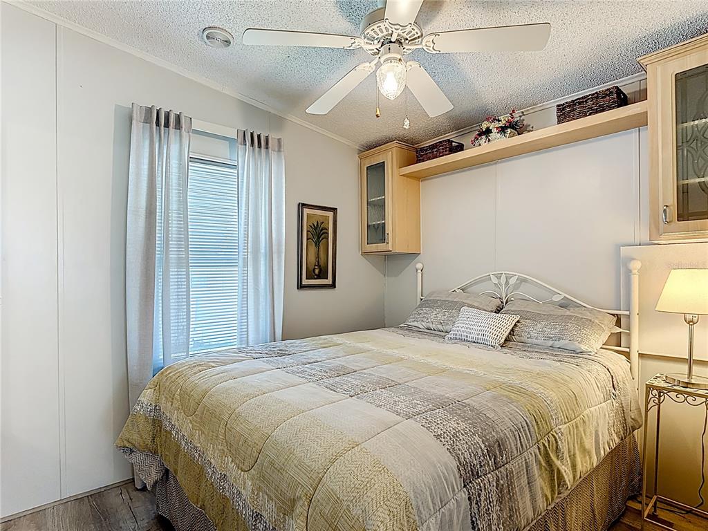 A bedroom features a bed with a patterned quilt, overhead cabinetry, and a ceiling fan — 9000 US HWY 192 # 545, CLERMONT, FL