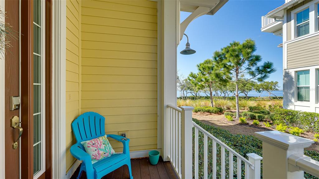 A blue chair sits on a covered porch with yellow siding overlooking a coastal landscape — 280 SAINT LUCIA DRIVE UNIT 101, BRADENTON, FL