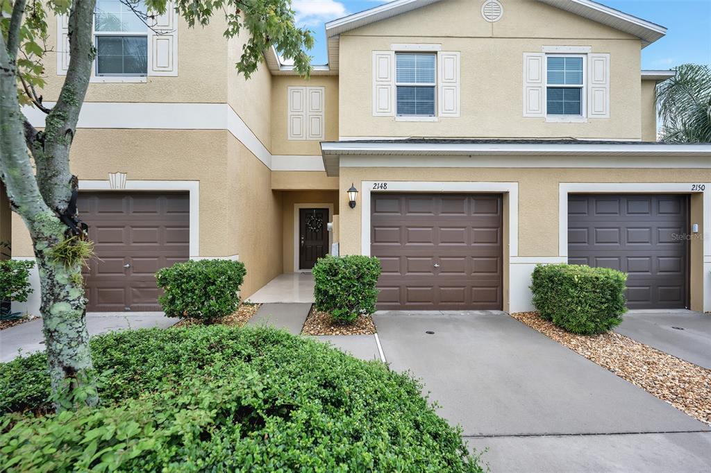 A two-story townhouse exterior features three brown garage doors and a central front entrance — 2148 GOLDEN FALCON DRIVE, RUSKIN, FL