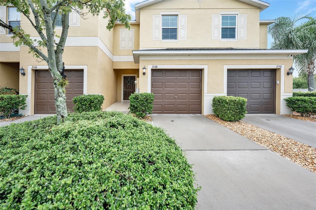 A multi-unit residential building with three garage doors and a large bush in the foreground — 2148 GOLDEN FALCON DRIVE, RUSKIN, FL