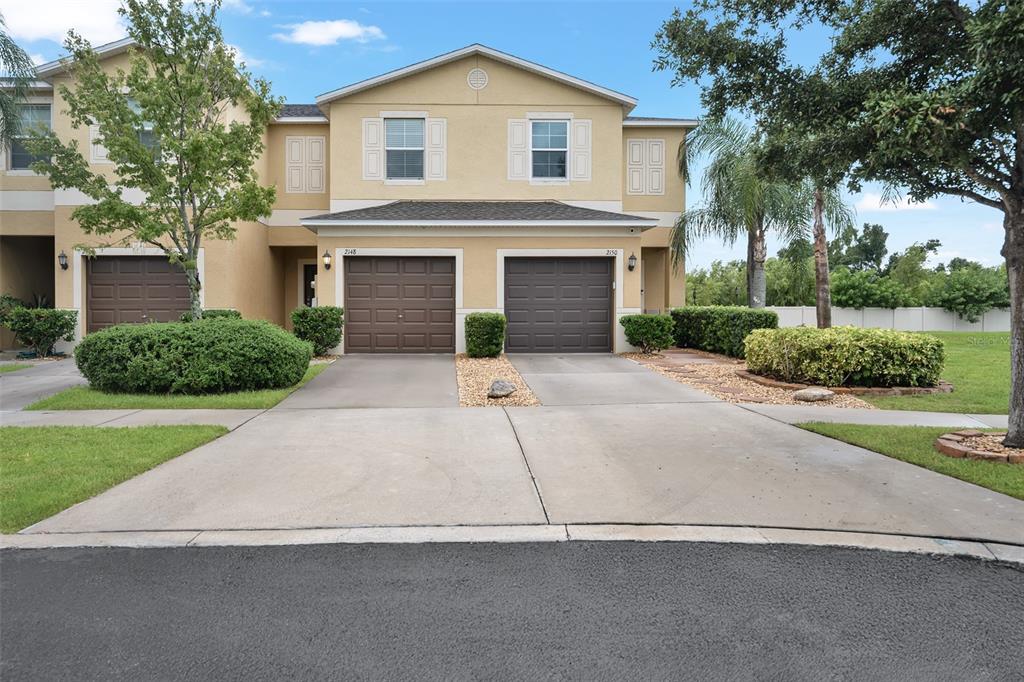 A two-story duplex with tan stucco siding, brown garage doors, and landscaped front yards — 2148 GOLDEN FALCON DRIVE, RUSKIN, FL