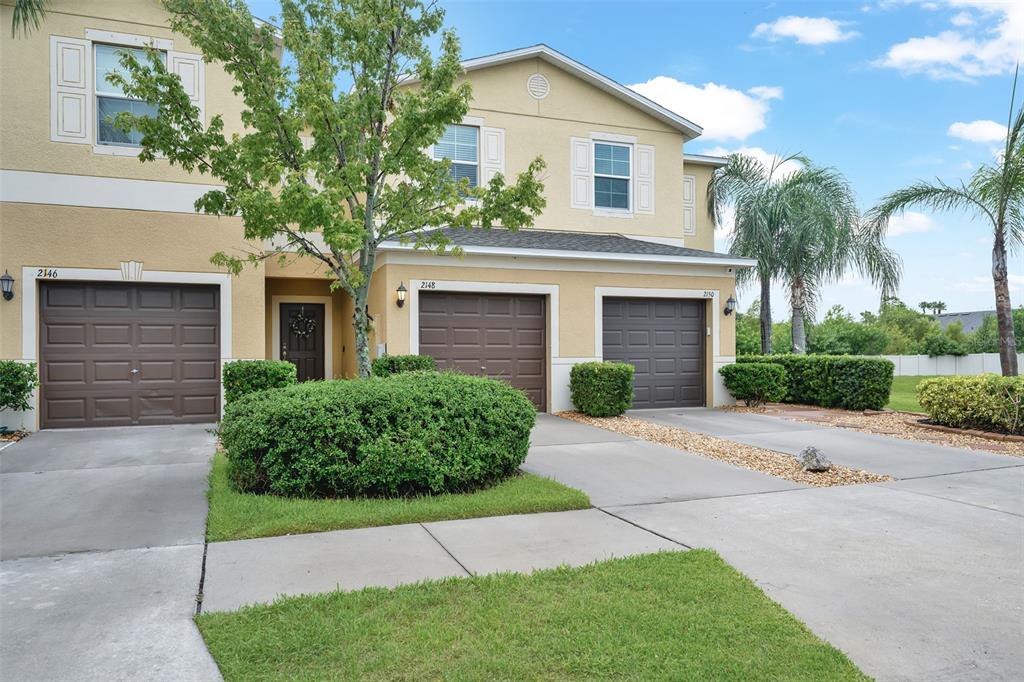 A multi-unit residential building features three garage doors, light-colored stucco walls, and landscaped front yards — 2148 GOLDEN FALCON DRIVE, RUSKIN, FL