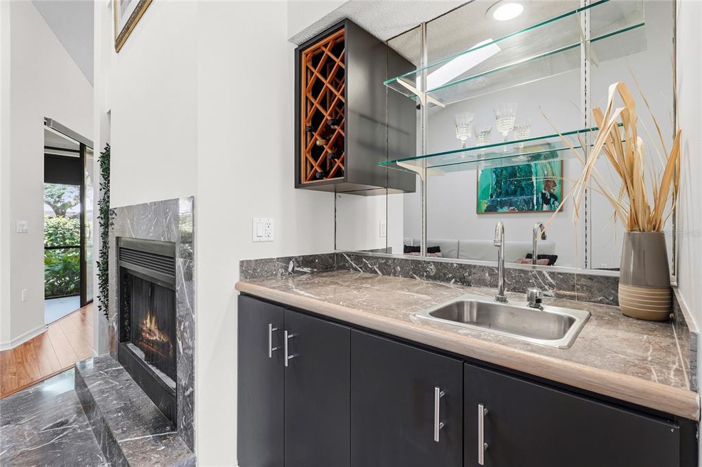 A wet bar with dark cabinets, marble countertops, and a wine rack next to a fireplace — 4531 LAS BRISAS LANE, SARASOTA, FL