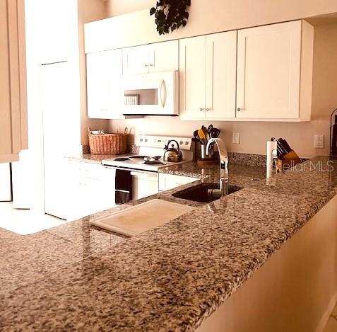 A kitchen features white cabinets, granite countertops, and stainless steel appliances — 9480 HIGH GATE DRIVE UNIT 2125, SARASOTA, FL