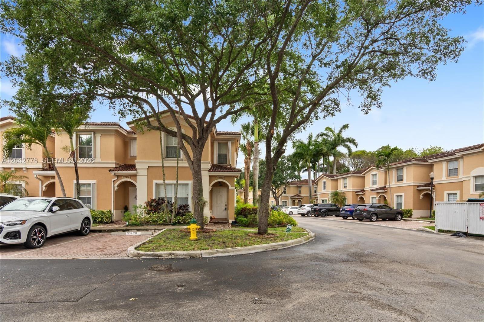 A row of two-story tan townhouses features paved driveways, mature trees, and a fire hydrant — 12990 SW 30th Ct # 150, Miramar FL 33027, MIRAMAR, FL