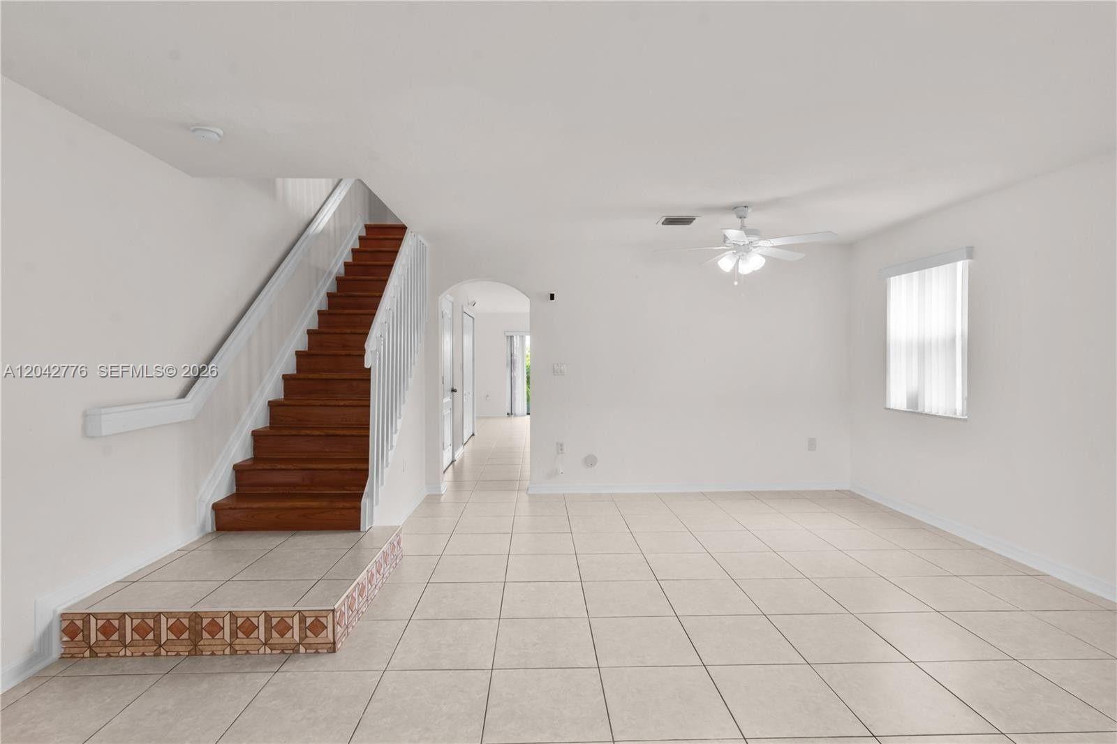 A living room features light tile flooring, white walls, and a wooden staircase — 12990 SW 30th Ct # 150, Miramar FL 33027, MIRAMAR, FL