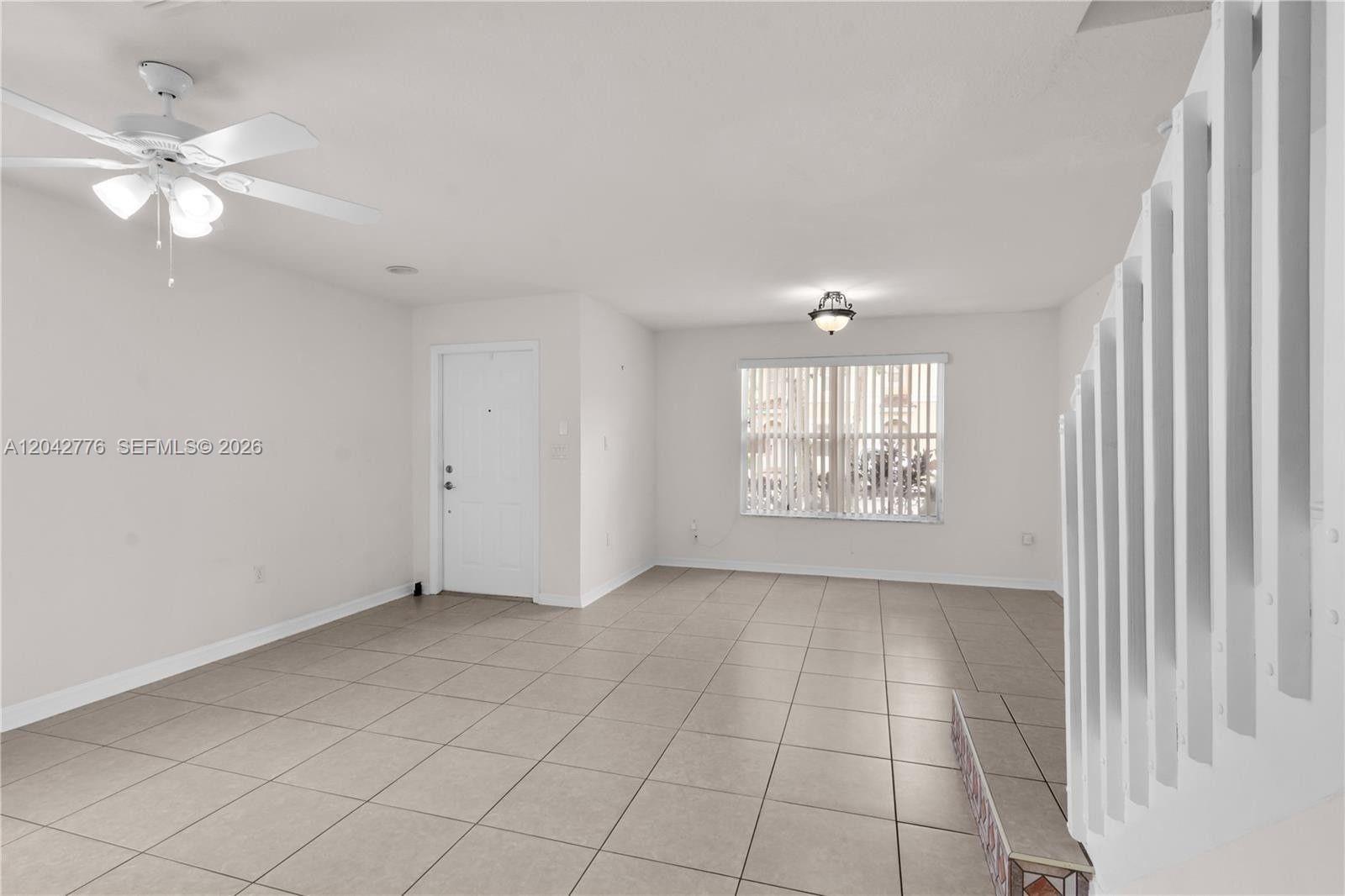 An empty living room features white walls, tile flooring, a ceiling fan, and a staircase — 12990 SW 30th Ct # 150, Miramar FL 33027, MIRAMAR, FL