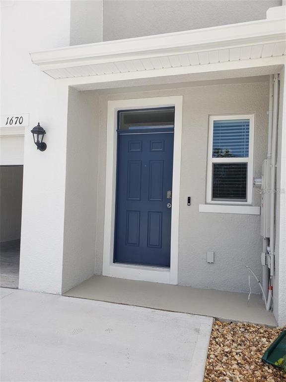 A blue front door is set into a white stucco exterior with a small porch — 1670 ROCK ELM ROAD, DAVENPORT, FL