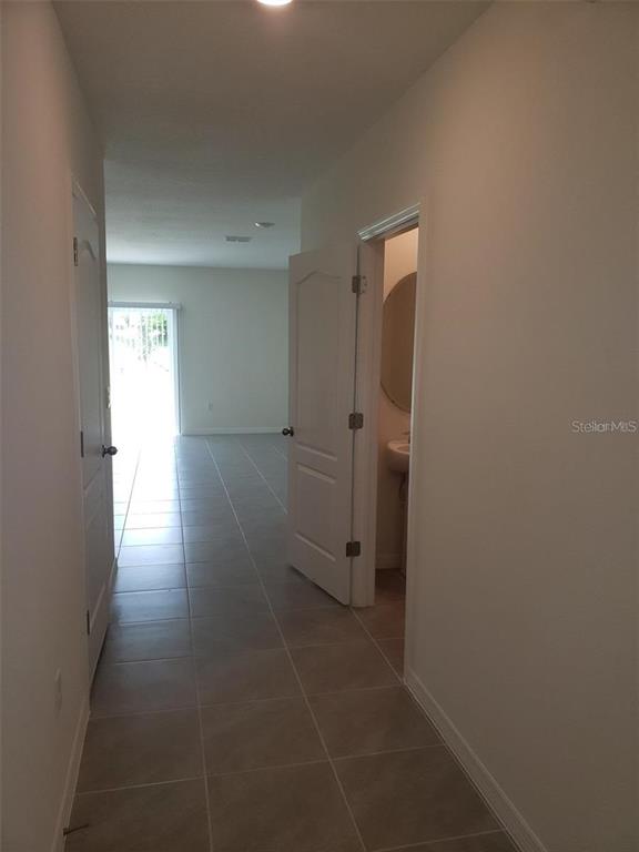 A hallway with tile flooring leads to a living area with a sliding glass door — 1670 ROCK ELM ROAD, DAVENPORT, FL