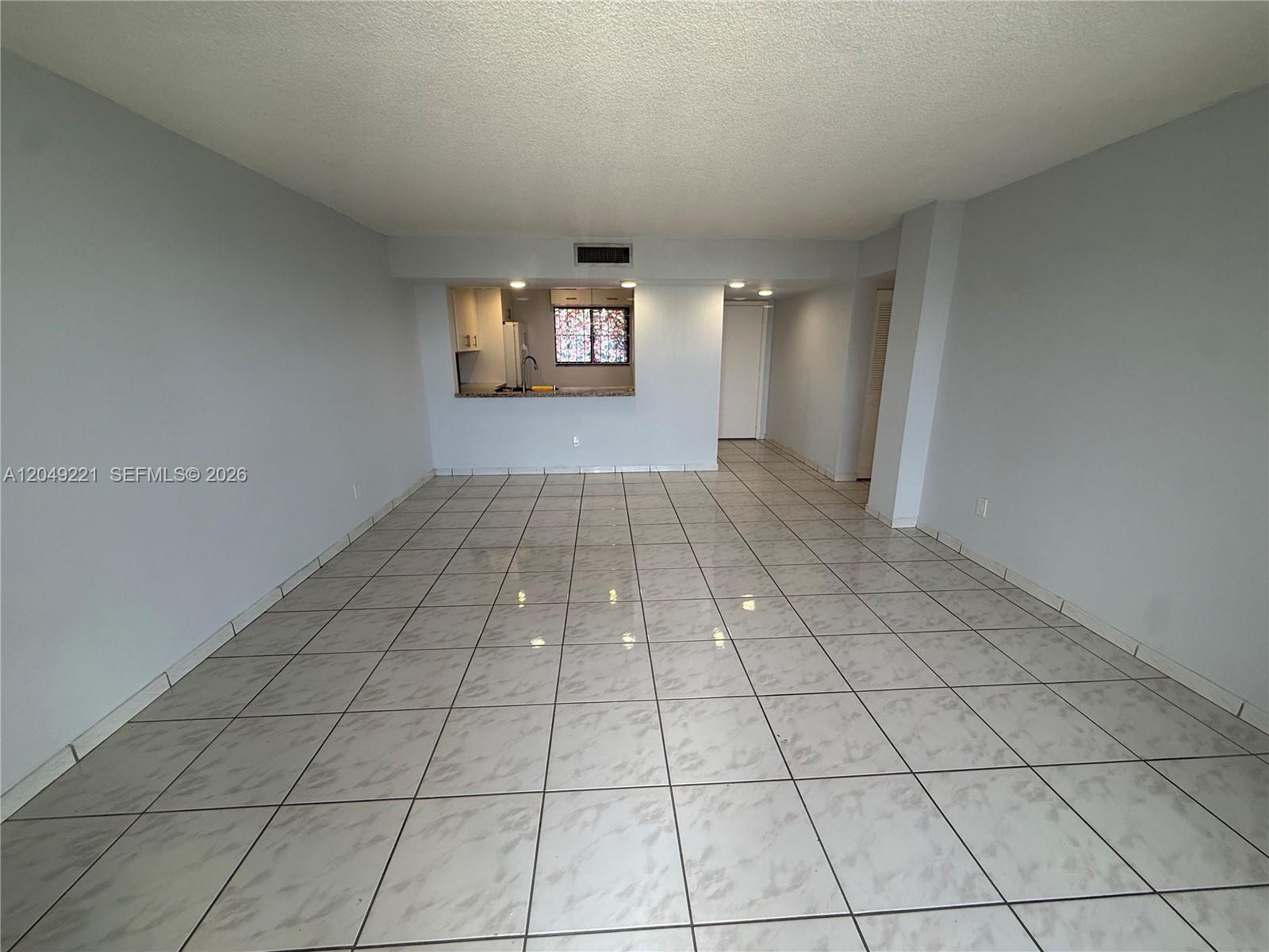 An empty living area features light-colored tile flooring and a pass-through window to the kitchen — 8625 NW 8th St # 420, Miami FL 33126, MIAMI, FL