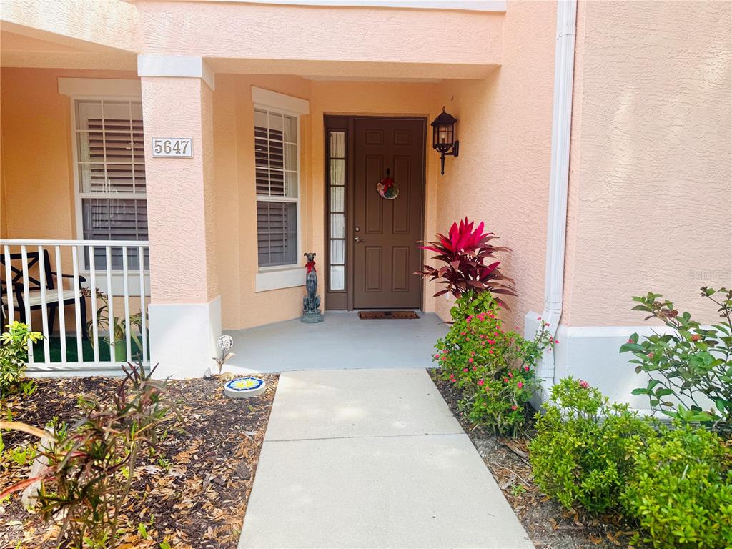 A concrete walkway leads to the front entrance of a peach-colored home with a door — 5647 KEY LARGO COURT UNIT C-07, BRADENTON, FL