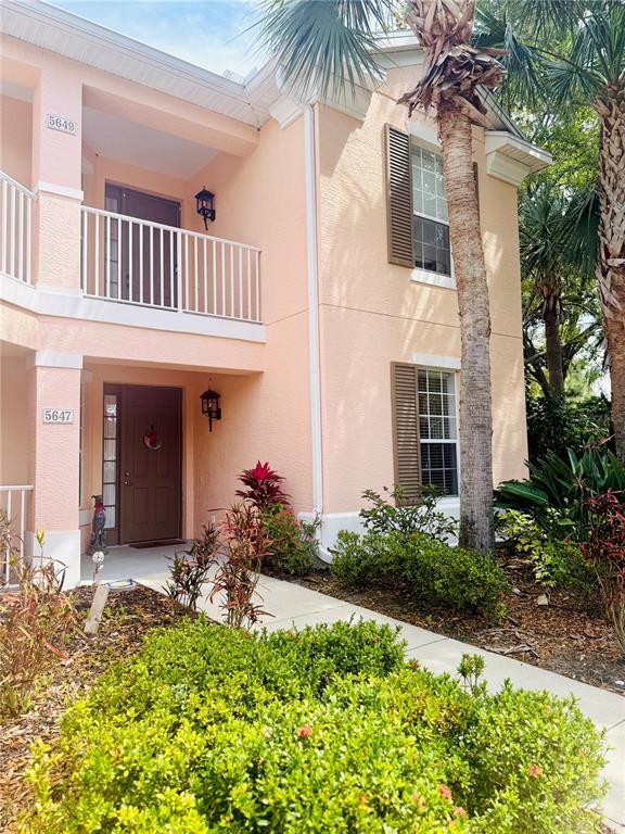 A two-story peach-colored building with a balcony, brown front door, and palm trees — 5647 KEY LARGO COURT UNIT C-07, BRADENTON, FL