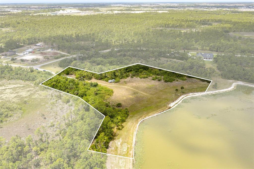 An aerial view shows a vacant, irregularly shaped lot bordering a lake and wooded area — FALCON COURT, VENICE, FL