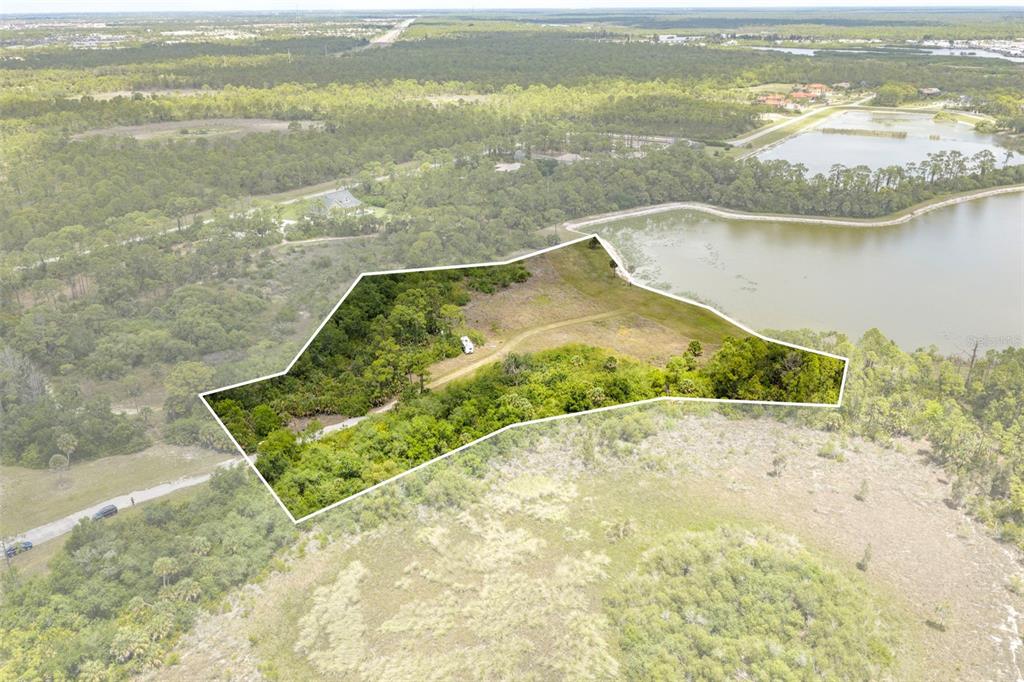 An aerial view shows a wooded, irregularly shaped plot of land bordering a large pond — FALCON COURT, VENICE, FL