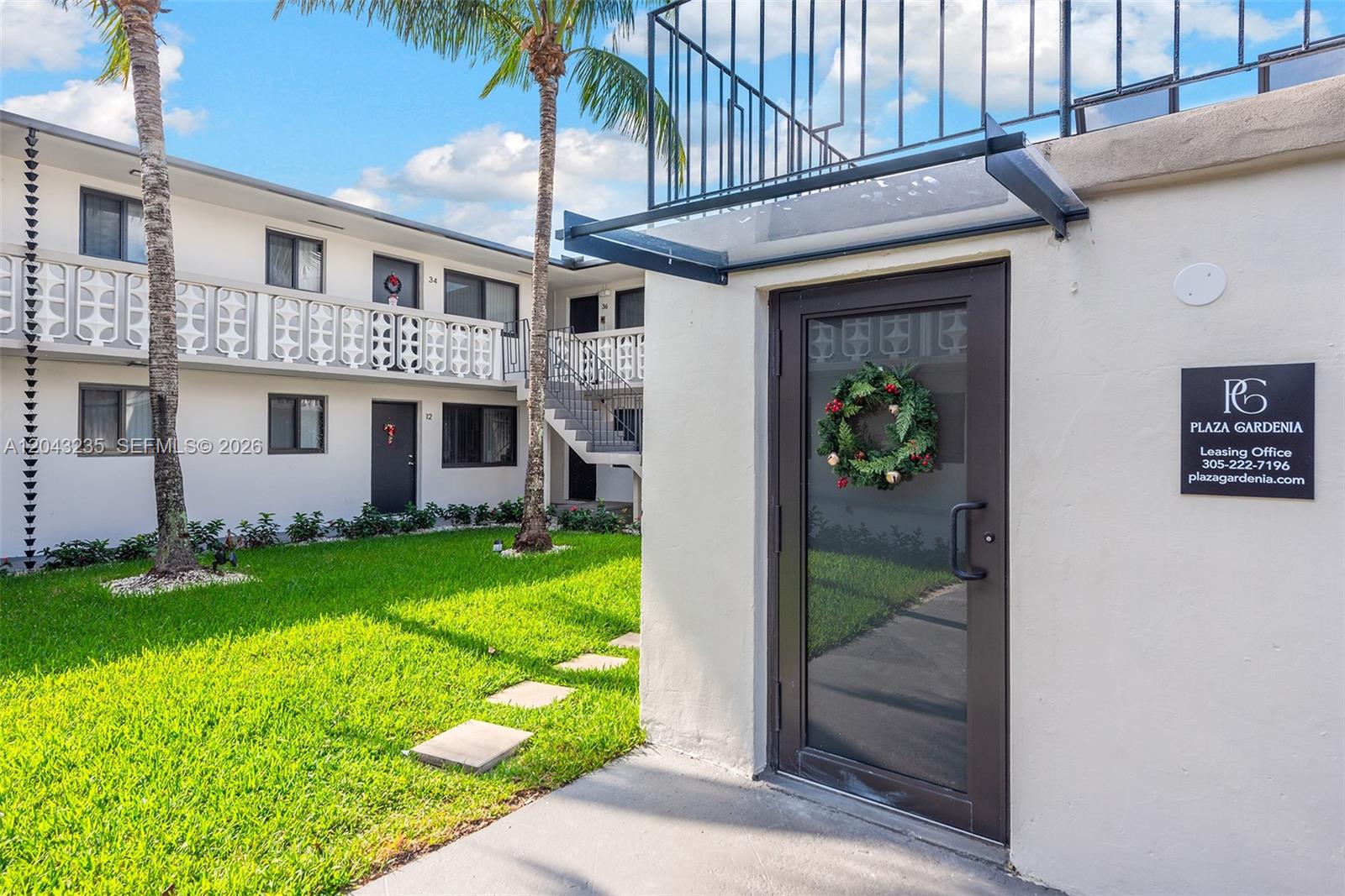 The exterior view shows a courtyard with a lawn, palm trees, and apartment building walkways — 1310 W 29th St # 40, Hialeah FL 33012, HIALEAH, FL