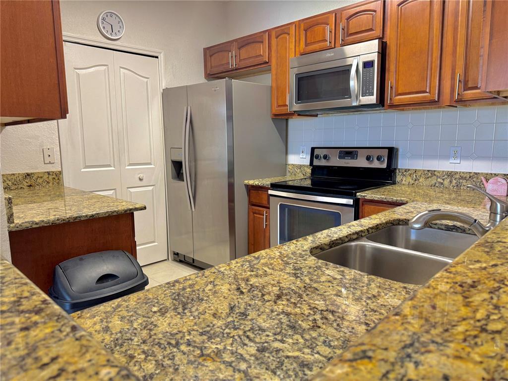 A kitchen features stainless steel appliances, wood cabinets, and speckled granite countertops — 8828 DUNES COURT UNIT 12 304, KISSIMMEE, FL