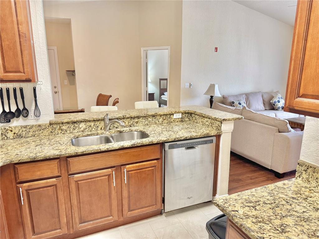 A kitchen with granite countertops and wood cabinets overlooks a living room with a sofa — 8828 DUNES COURT UNIT 12 304, KISSIMMEE, FL
