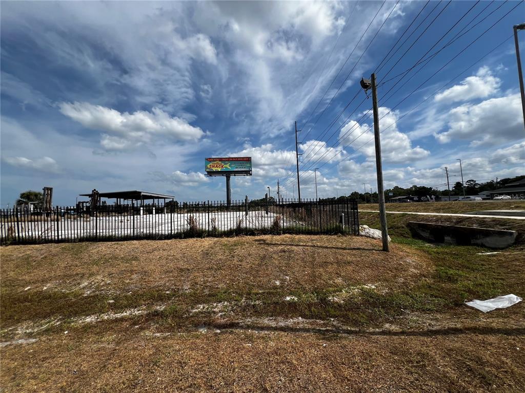 A fenced, vacant lot features a billboard and a small covered structure under a cloudy sky — 6919 PUFFIN LANE, HUDSON, FL