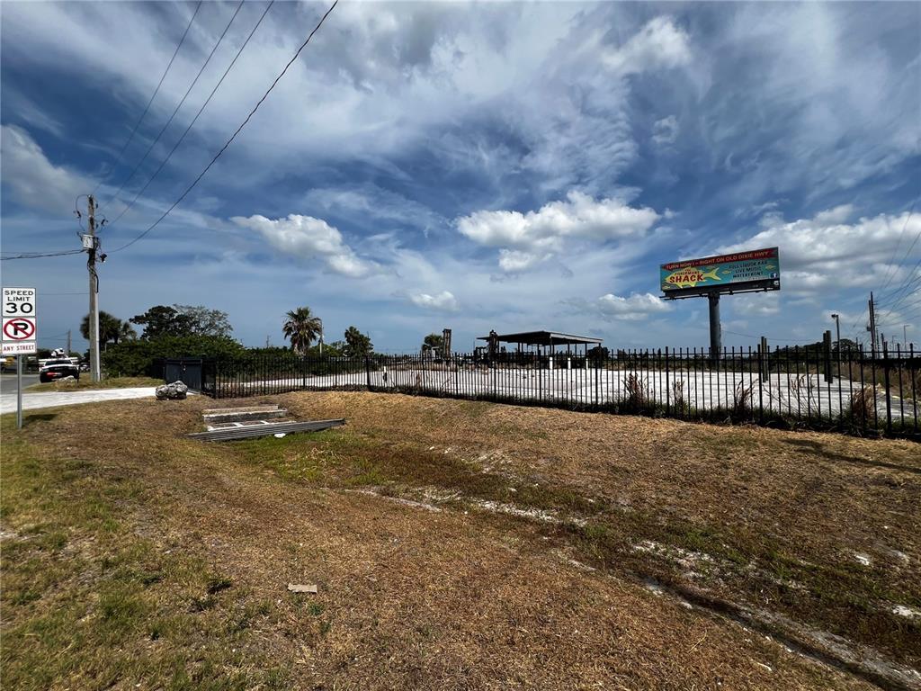 A fenced, vacant lot features a covered structure and a large billboard under a cloudy sky — 6919 PUFFIN LANE, HUDSON, FL