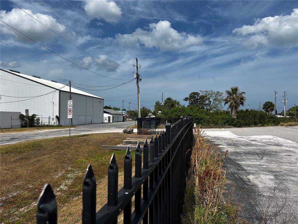 A black metal fence borders a paved lot next to a large industrial building — 6919 PUFFIN LANE, HUDSON, FL