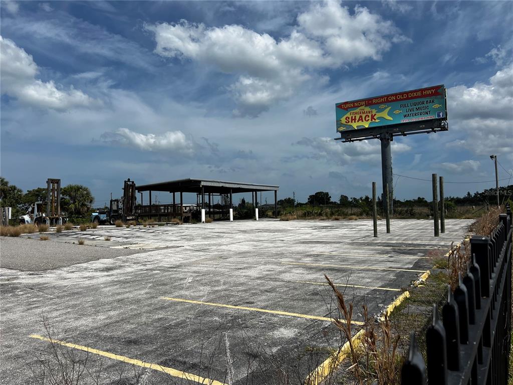 A large, empty paved parking lot features a covered structure and a prominent billboard sign — 6919 PUFFIN LANE, HUDSON, FL