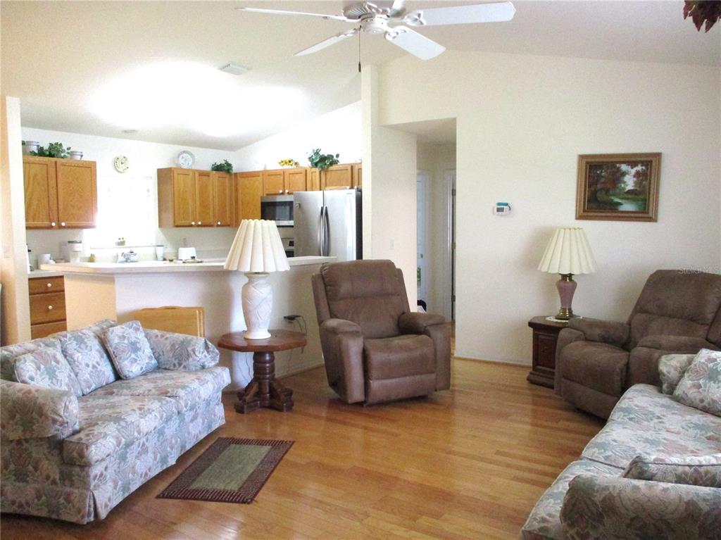 A living room with hardwood floors, two floral sofas, two recliners, and an open kitchen — 11588 SW 139TH PLACE, DUNNELLON, FL
