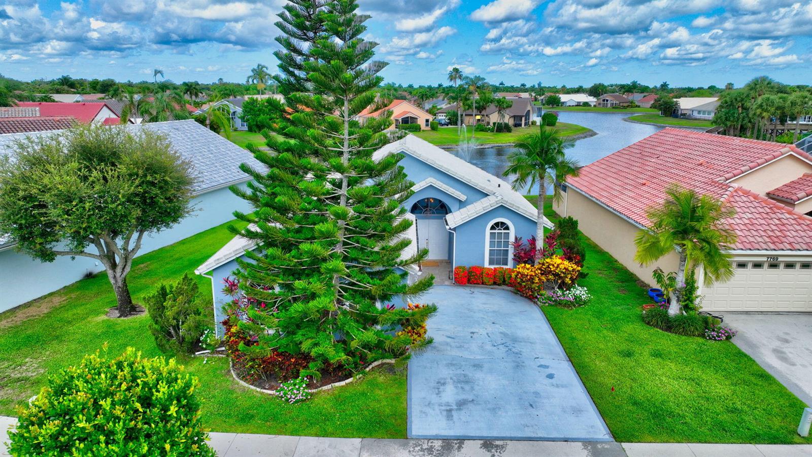 An aerial view of a blue house with a large pine tree and a lake — 7777 Stirling Bridge Boulevard S, Delray Beach FL 33446, DELRAY BEACH, FL
