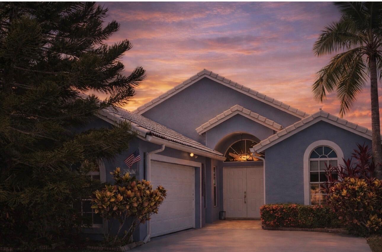 A blue single-story house with a two-car garage and palm tree at sunset — 7777 Stirling Bridge Boulevard S, Delray Beach FL 33446, DELRAY BEACH, FL