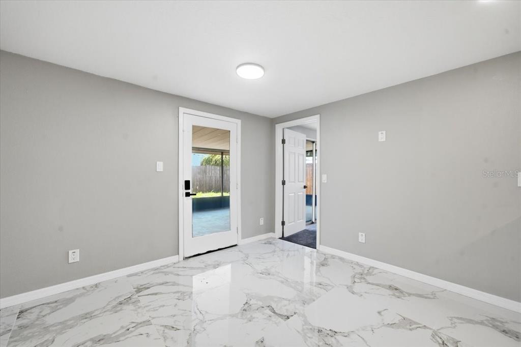 A room with gray walls, white marble-look tile flooring, a glass door, and a doorway — 6224 KELLER DRIVE UNIT 1, PORT RICHEY, FL