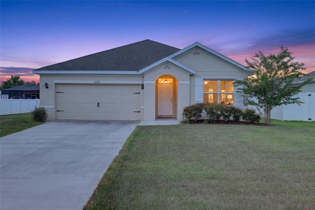 A single-story house with a beige stucco exterior, a two-car garage, and a front lawn — 3886 SE 97TH LANE, BELLEVIEW, FL