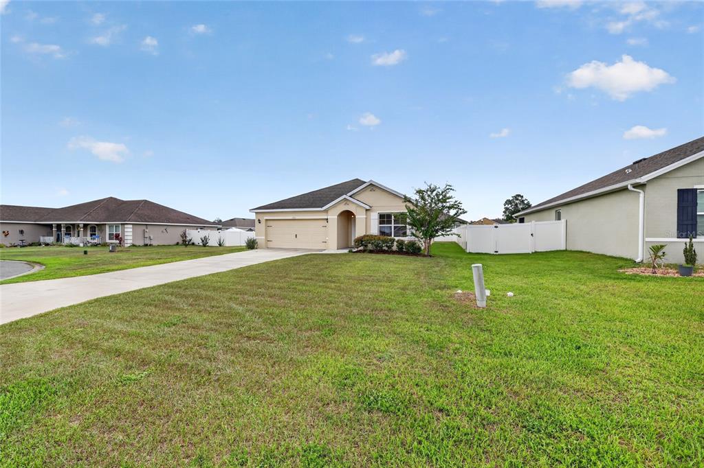 A single-story house with a beige exterior, a two-car garage, and a large front lawn — 3886 SE 97TH LANE, BELLEVIEW, FL