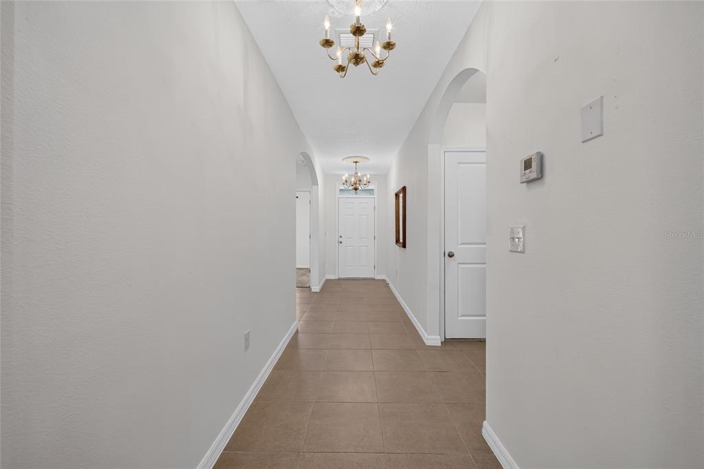 A tiled hallway leads to a front door with two chandeliers hanging from the ceiling — 3886 SE 97TH LANE, BELLEVIEW, FL