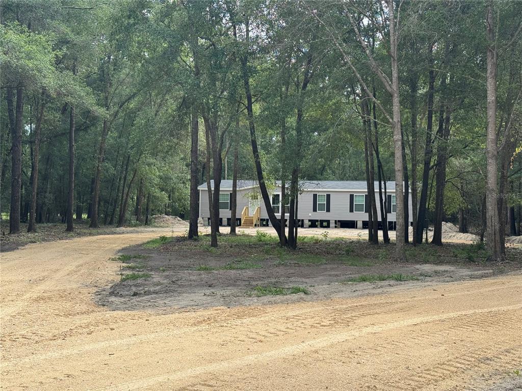 A light-colored manufactured home sits among trees at the end of a dirt driveway — 17790 NW 266TH STREET, HIGH SPRINGS, FL