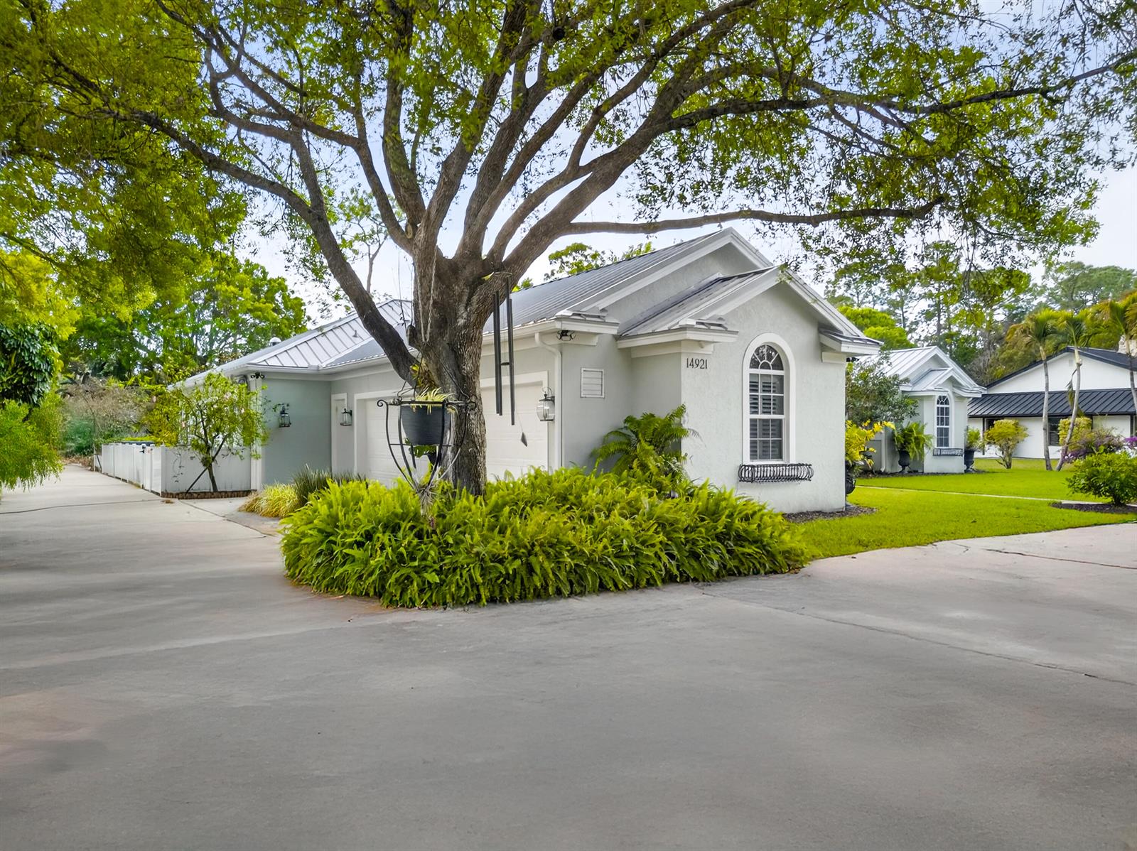 A light-colored house with a metal roof features a large tree and lush landscaping — 14921 Horseshoe Trace, Wellington FL 33414, WELLINGTON, FL