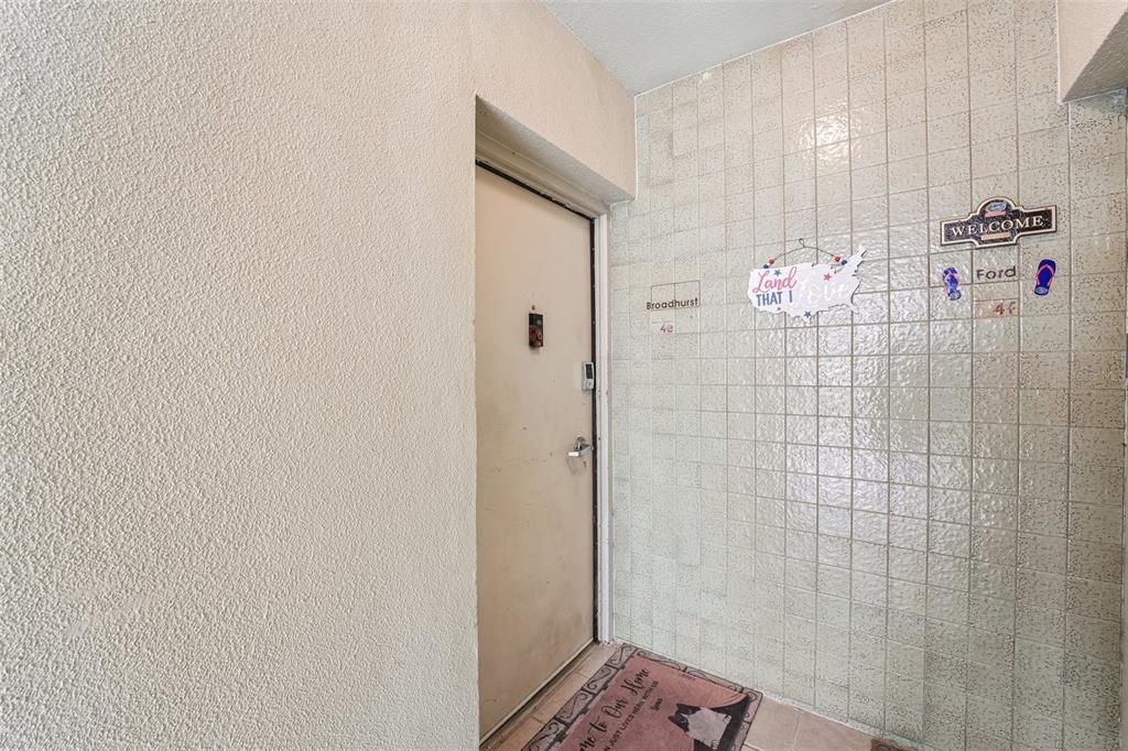 A beige door with a welcome mat sits in a tiled entryway with textured walls — 1717 NW 23RD AVENUE UNIT 4E, GAINESVILLE, FL